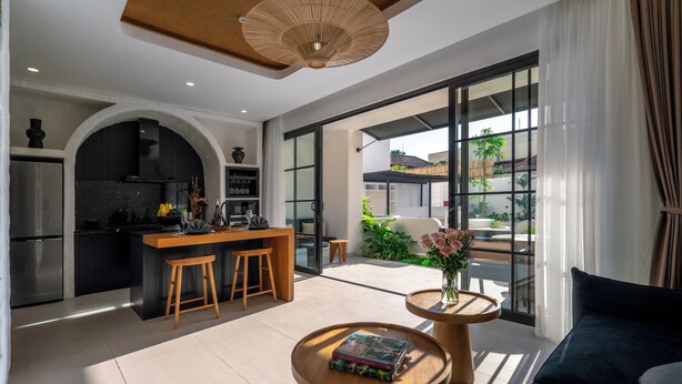 Una cocina moderna con una isla central, un área de comedor con sofá y mesa de centro, y ventanas amplias que ofrecen vistas al exterior.