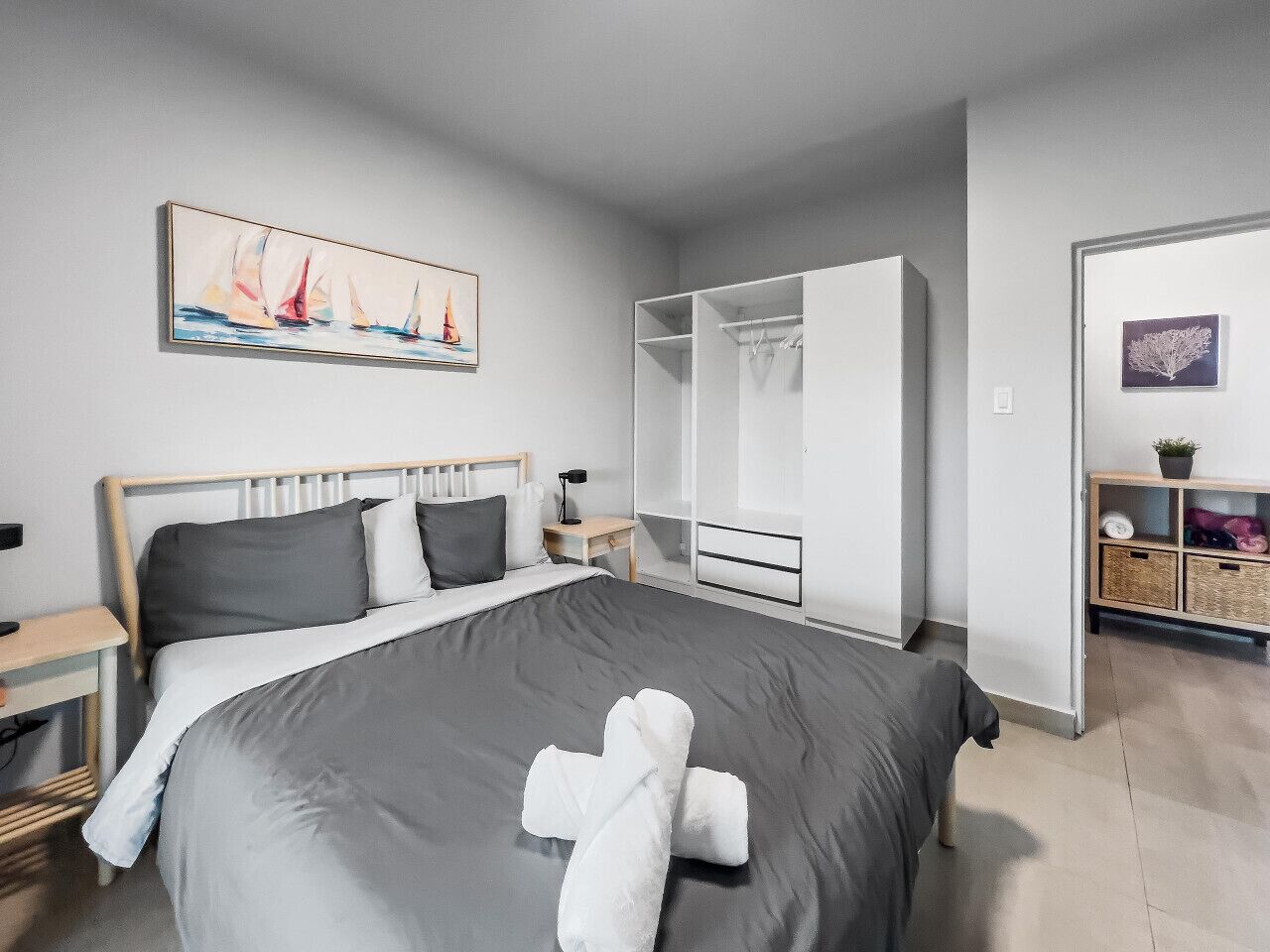 A modern bedroom with a large bed, a wardrobe, a nightstand, and a painting on the wall.