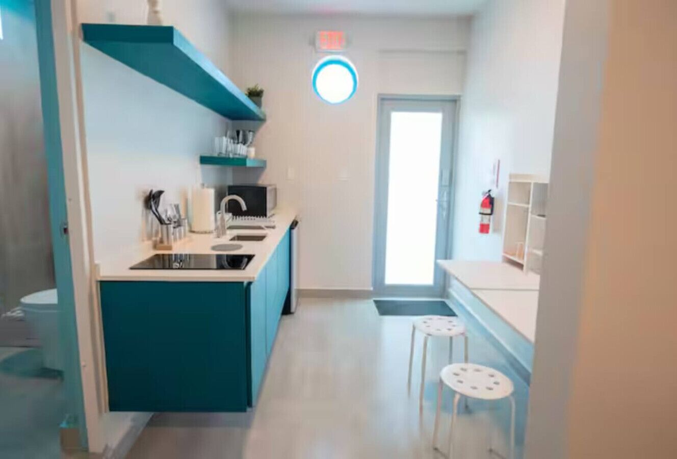 A compact kitchen with teal cabinetry, a sink, and two stools.