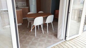 Kompakti keittiö, jossa on jääkaappi, puukaapit sekä ruokailutila, jossa on pöytä ja tuolit.
