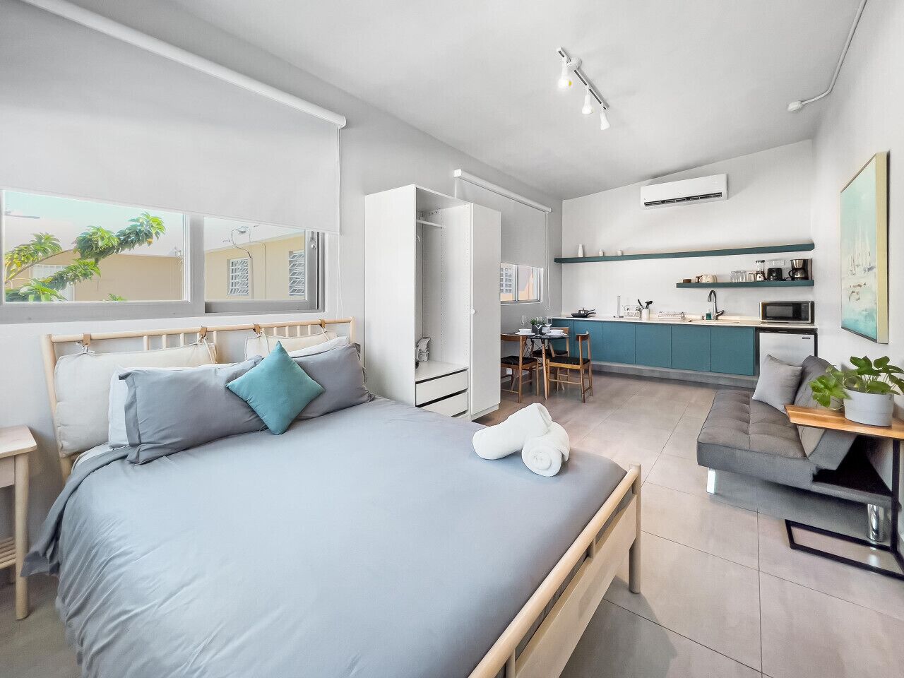 A modern bedroom with a large bed, a desk, and a kitchenette.