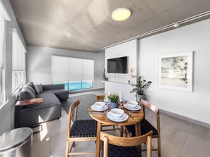 Una sala de estar moderna con comedor, un sofá gris, un televisor de pantalla plana y vista al océano.