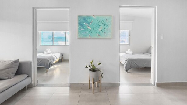 Une chambre moderne et minimaliste, avec deux lits, un canapé gris et une petite table agrémentée d’une plante.