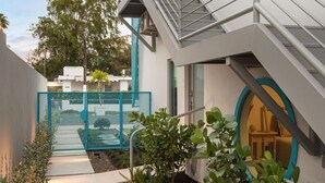 A modern building with a staircase leading to a balcony, surrounded by a garden with various plants and a blue fence. - Aquabella #8 - Beach Bliss in Isla Verde (Carolina)