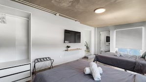 A modern hotel room with two beds, a TV, a small plant, and a view of the city. - Aquabella #8 - Beach Bliss in Isla Verde (Carolina)