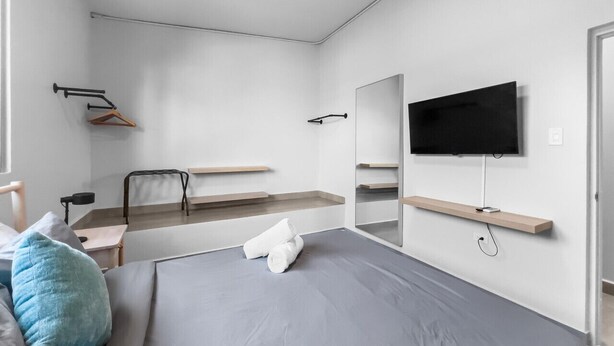 A modern hotel room with a bed, a TV mounted on the wall, a mirror, and a small desk with a chair. - Aquabella #8 - Beach Bliss in Isla Verde (Carolina)