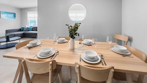 A modern dining area with a wooden table set for six, surrounded by chairs. A vase with greenery is placed in the center. - Aquabella #8 - Beach Bliss in Isla Verde (Carolina)