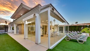 Ein modernes Haus mit einer verglasten Terrasse, Sitzgelegenheiten im Freien und einem gepflegten Rasen.