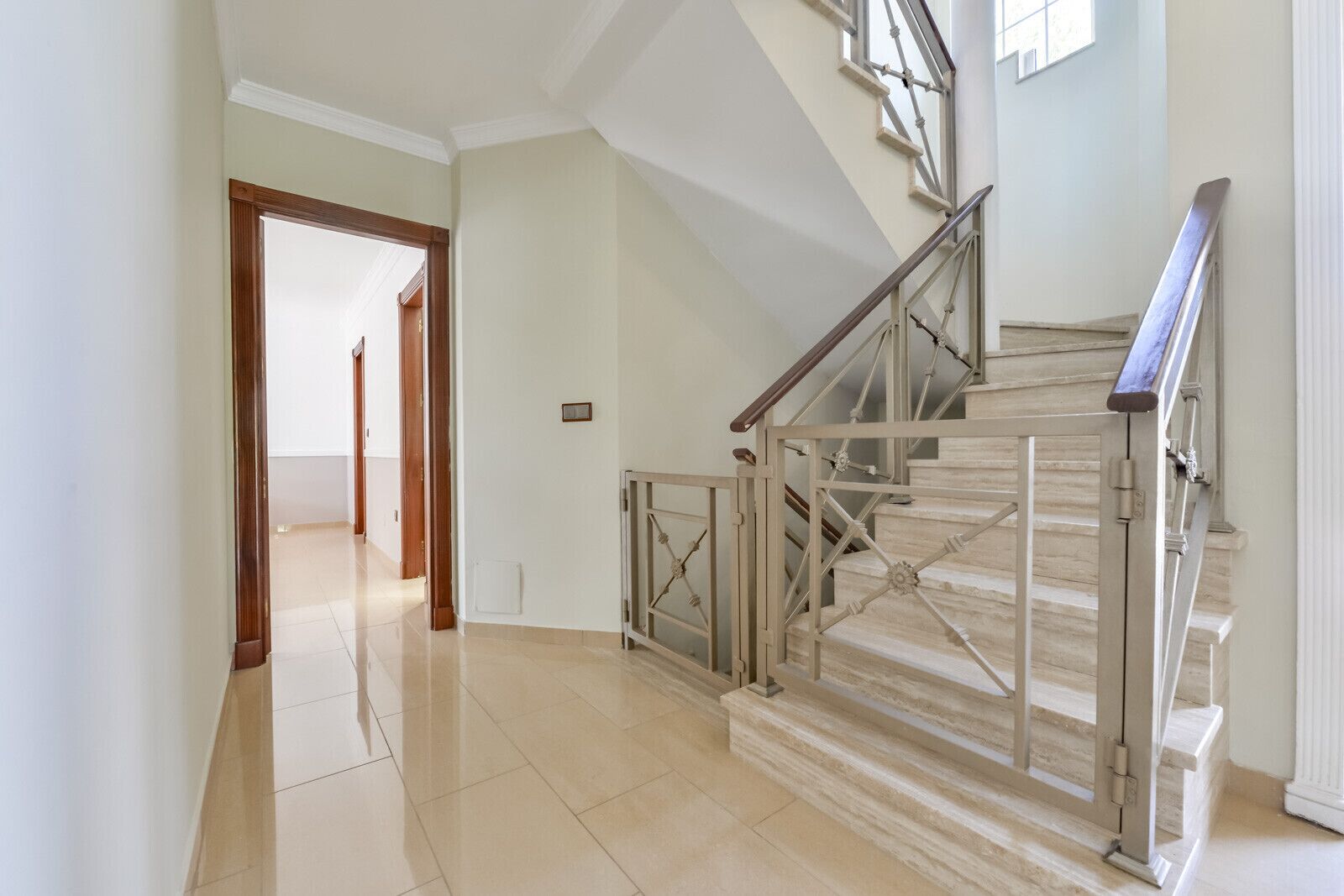 Un hall d’entrée spacieux, doté d’un plancher poli, mène à un escalier avec une rampe en métal et des marches en bois.