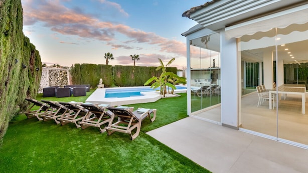 Ein modernes Haus mit Swimmingpool, Außenbereich mit Sitzgelegenheiten und einem wintergartenartigen Essbereich.