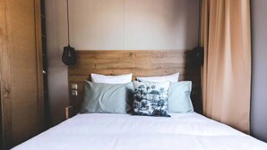 Een bed met witte lakens, een houten hoofdbord en twee hangende lampen.
