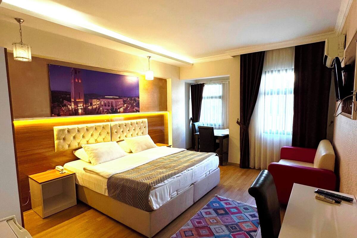 A modern hotel room with a large bed, a desk, a chair, and a small table.