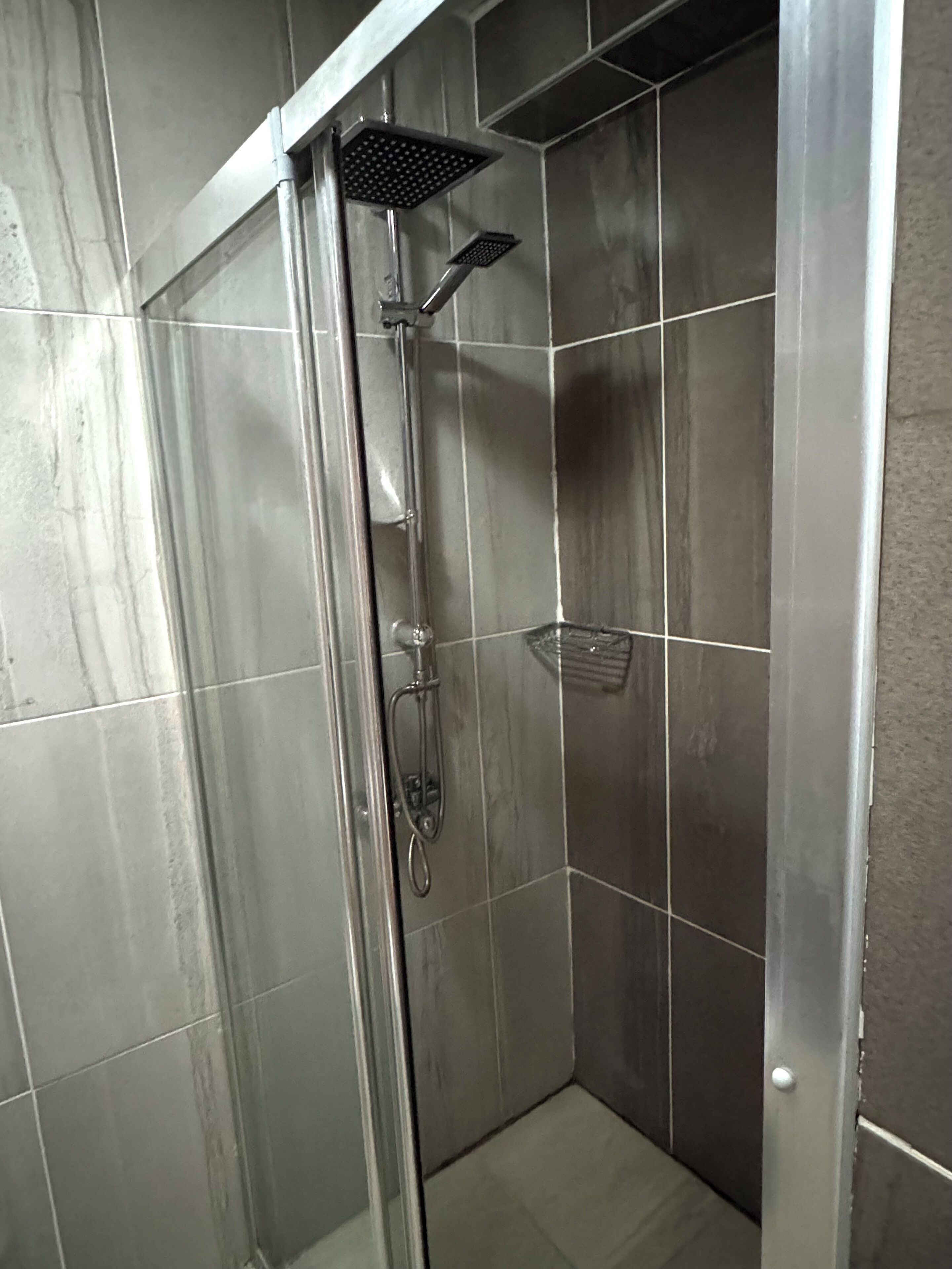 A modern shower with a glass door, a handheld showerhead, and a wall-mounted showerhead.