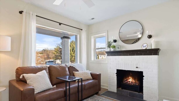 A living room with a fireplace, a sofa, a coffee table, and a view through a large window. - Mountain View Cottage | Walk to Town | Pet (Shenandoah)
