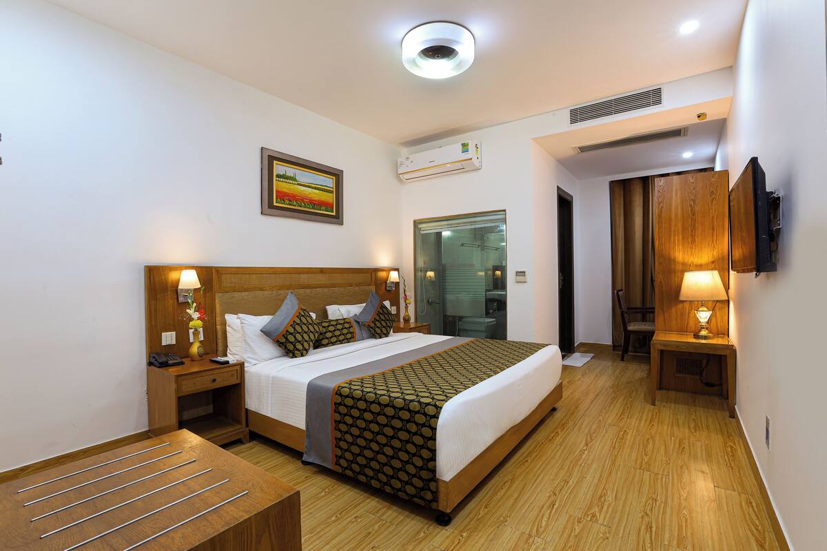 A hotel room with a wooden bed, bedside tables, a desk, and a TV mounted on the wall.