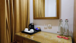 A hotel room with a wooden desk, a coffee maker, two bottles, and a mirror. - OPO PREMIER (New Delhi)