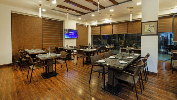 A spacious dining area with multiple tables and chairs, wooden flooring, and ceiling beams. - OPO PREMIER (New Delhi)