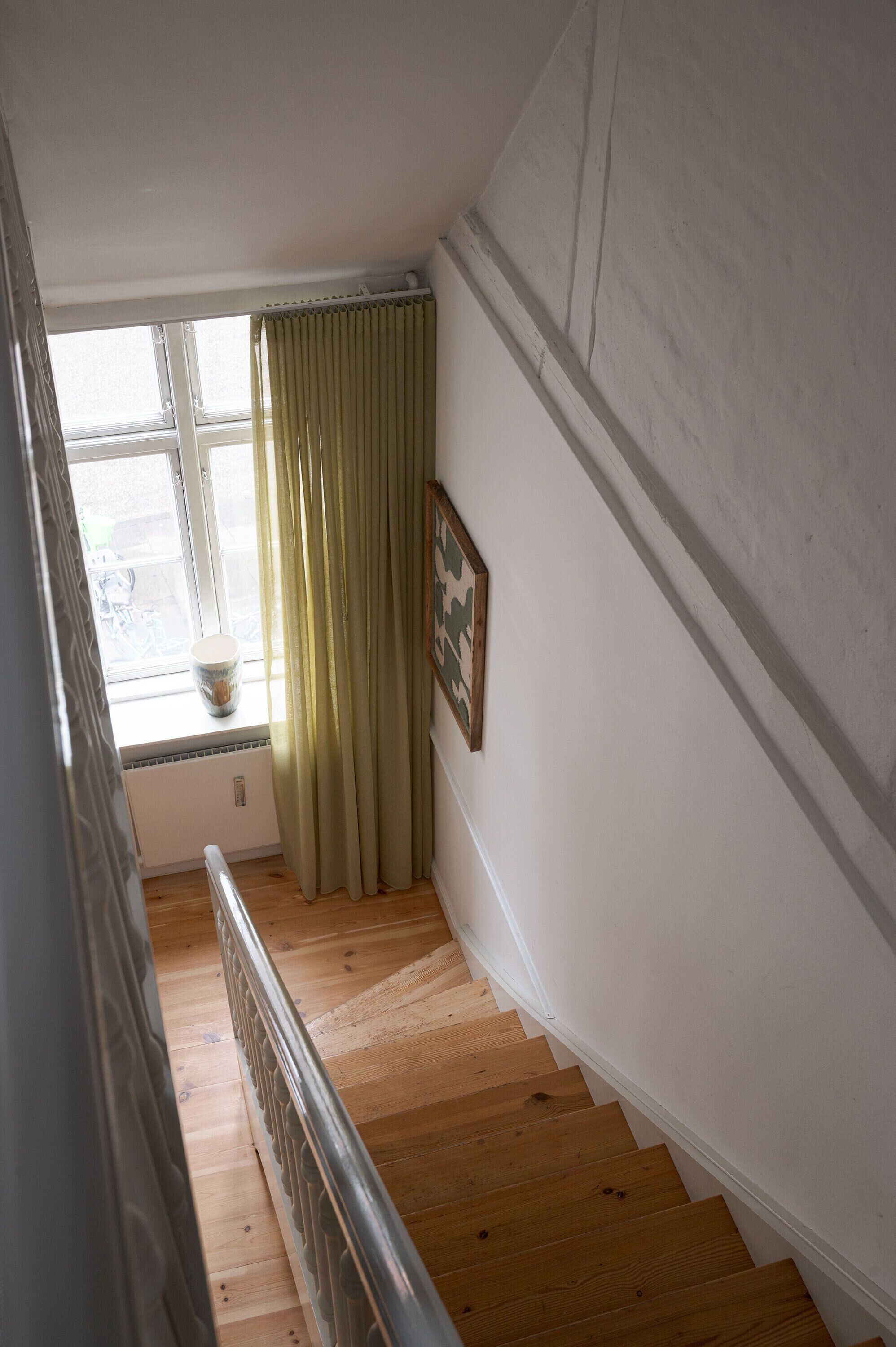 A wooden staircase with a radiator and a window with curtains.