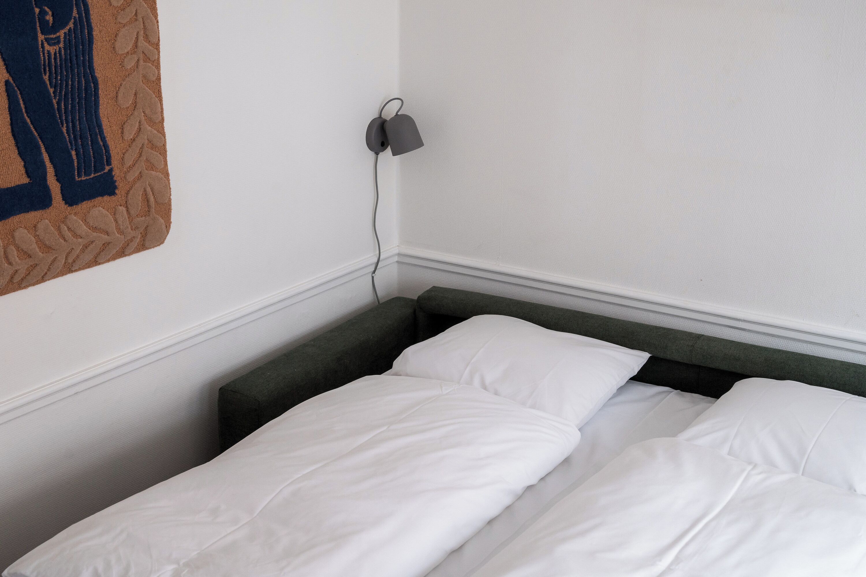 Cama bem arrumada com roupa de cama branca em um quarto com parede branca e cabeceira verde escura.