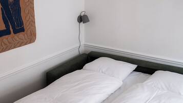 Cama bem arrumada com roupa de cama branca em um quarto com parede branca e cabeceira verde escura.