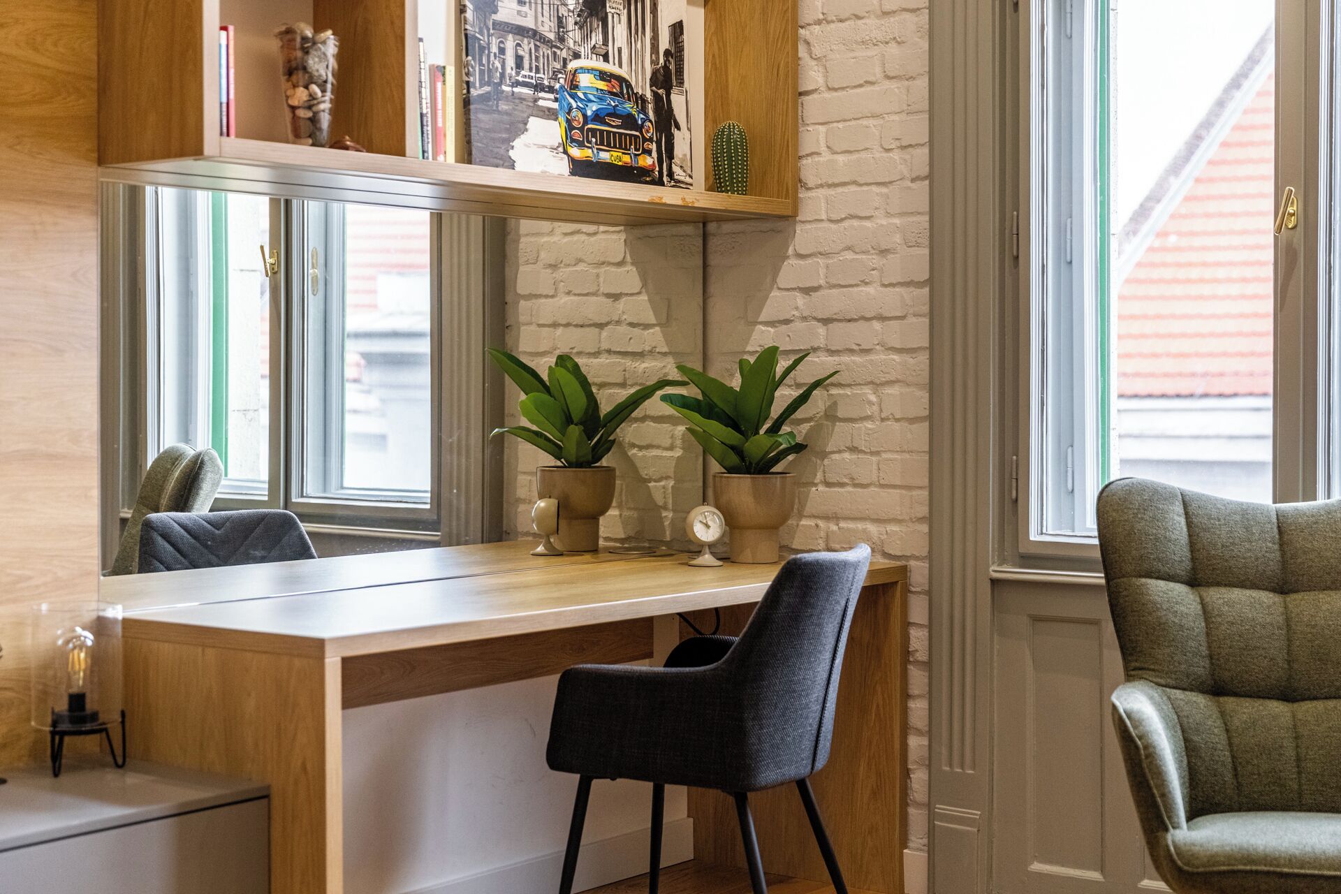 A room with a wooden desk, two chairs, a potted plant, a clock, and a window with a view of buildings.