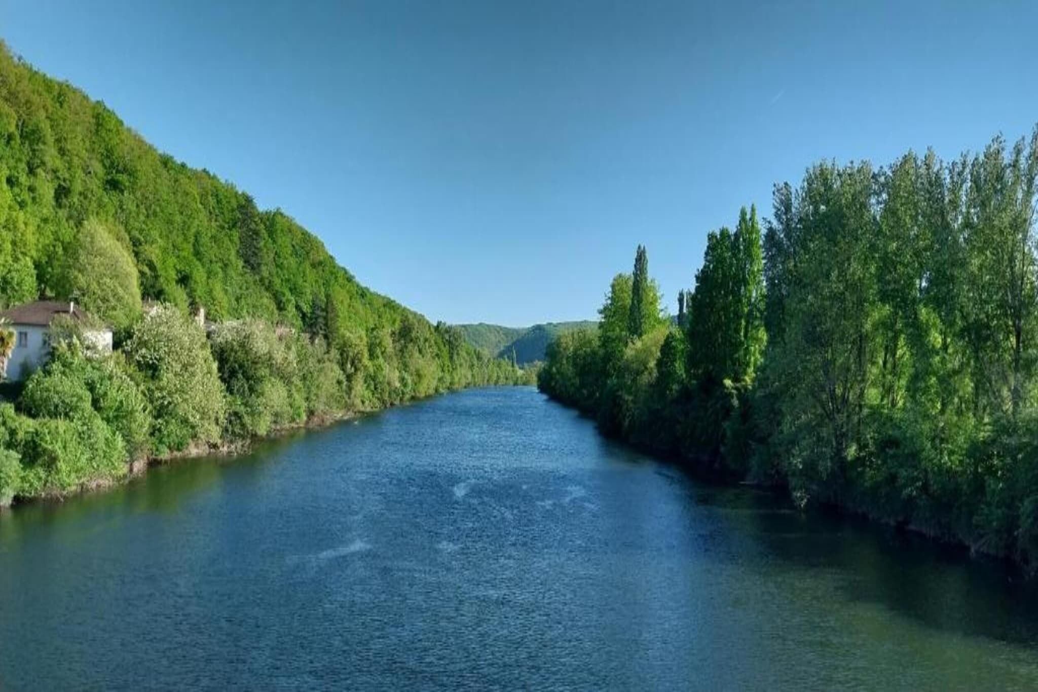 Un río flanqueado por abundante vegetación y una casa a la izquierda.