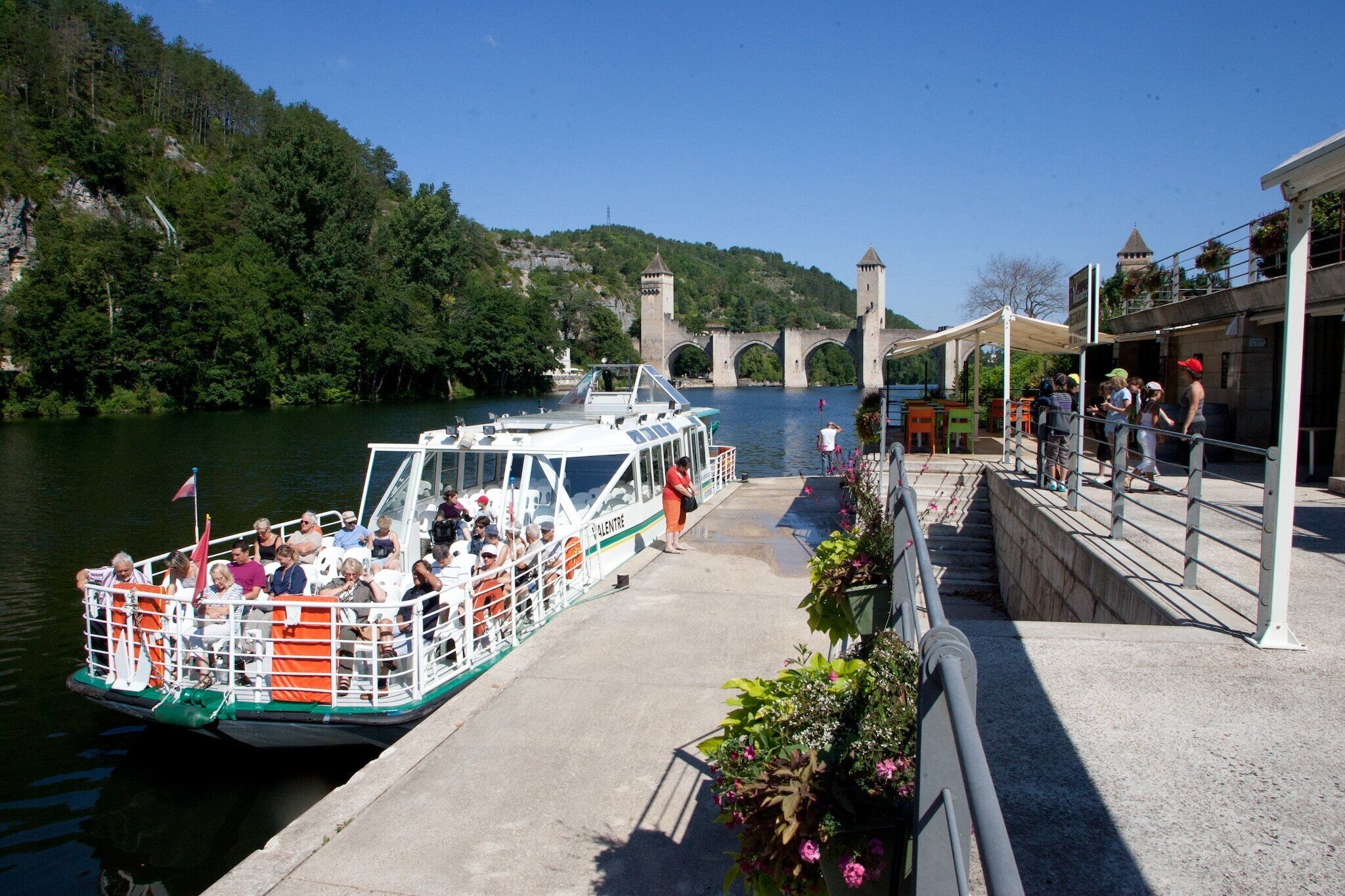 Un bateau était amarré à un quai, des passagers s’y trouvaient, et un pont se dressait en arrière-plan.