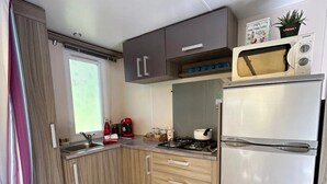 Une cuisine de taille réduite équipée d’un réfrigérateur, d’une cuisinière, d’un four à micro-ondes et de meubles de rangement en bois.