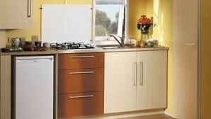 A compact kitchen with a dishwasher, a stove, and a window with blinds. - ZEcamping 3 étoiles animé piscine chauffée dog friendly locatif BBQ (Mondragon)
