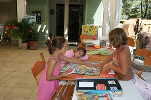 Eine Gruppe Kinder spielt an einem Tisch im Freien ein Brettspiel.