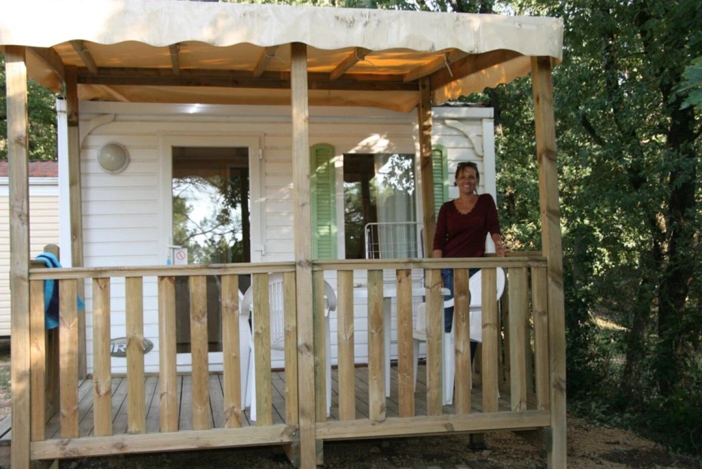 Eine Holzdiele mit einer überdachten Veranda, ein weißes Gebäude mit grünen Fensterläden und eine Person, die auf der Veranda steht.