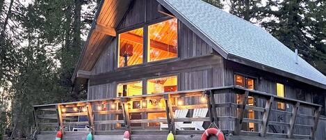 A wooden cabin with a sloped roof, large windows, and a deck with colorful life rings.