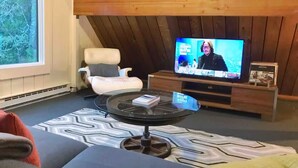 Un accogliente soggiorno con televisione, una poltrona bianca e un tappeto decorato.