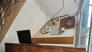 A reception desk with a laptop, a wooden panel wall, visible electrical wiring, and a window. - Divy Dhaam Near Prem Mandir (Vrindavan)