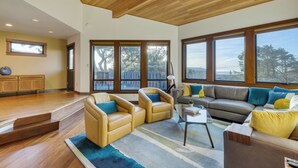 Un salon spacieux avec un plafond en bois, de grandes fenêtres et une vue sur l’extérieur.