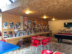 Una biblioteca con scaffali, un tavolo da biliardo e una televisione.