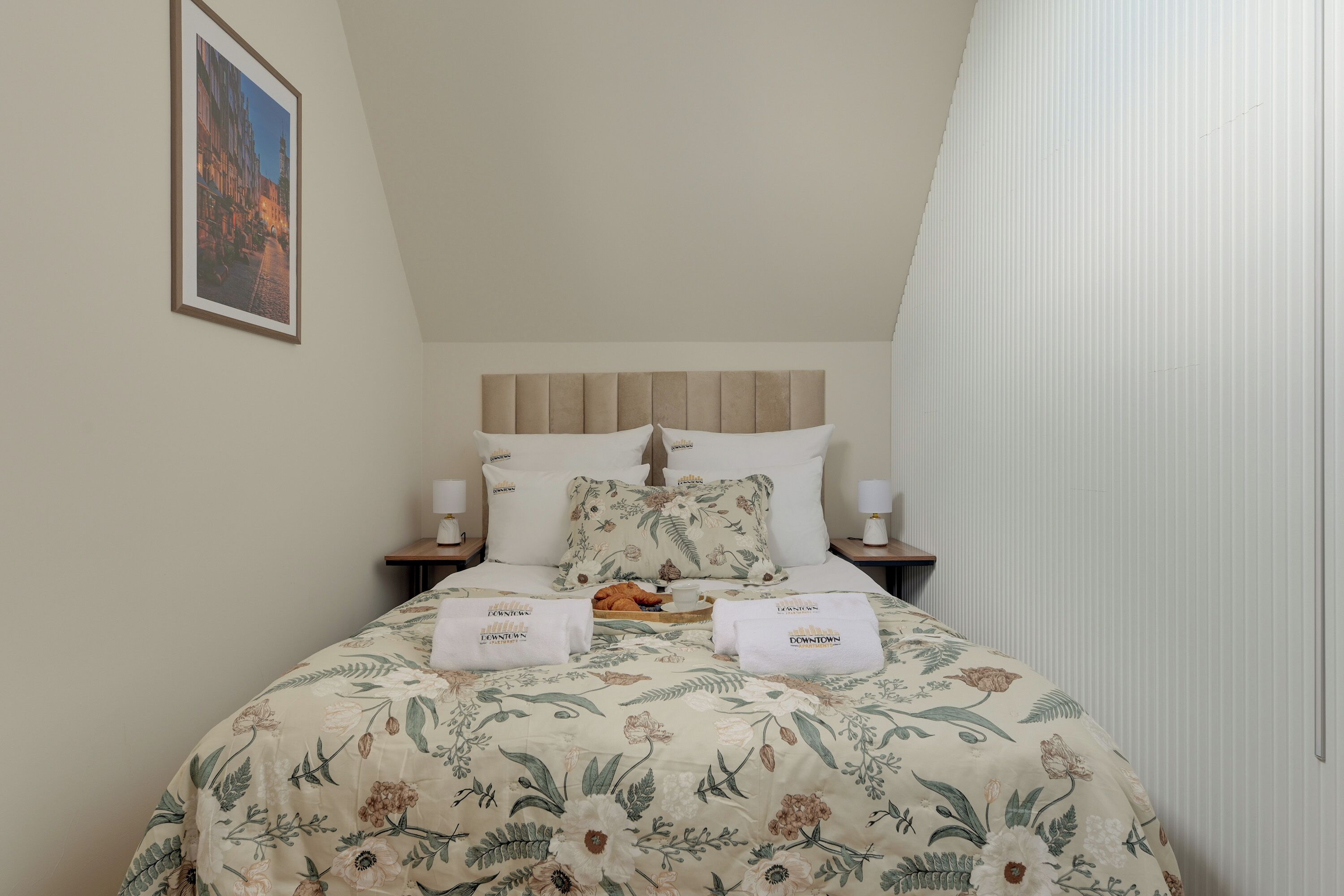 Habitación de hotel con cama, dos mesitas de noche, un cuadro enmarcado en la pared y una ventana con cortinas.
