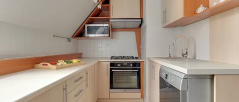 A compact kitchen with built-in appliances, wooden cabinetry, and a white countertop.