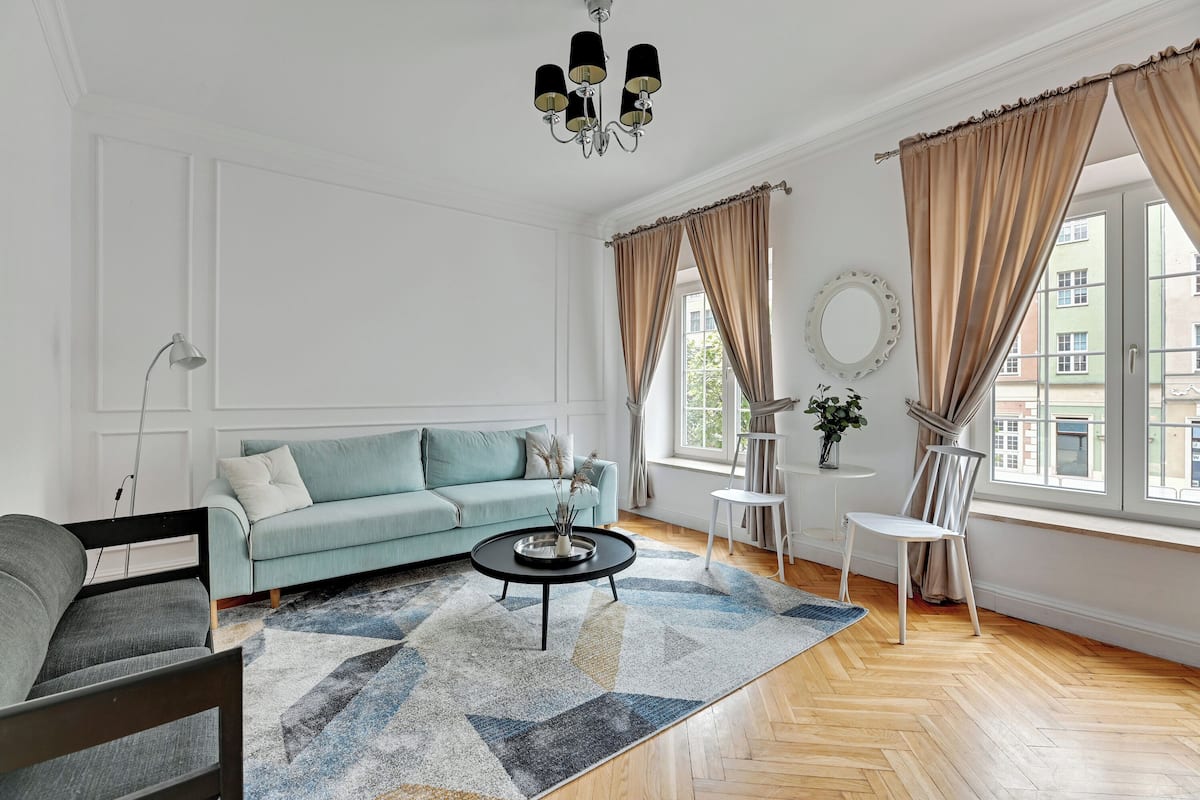 Un salón con un sofá azul claro, una mesa de centro redonda y un suelo de madera con patrón de espiga.