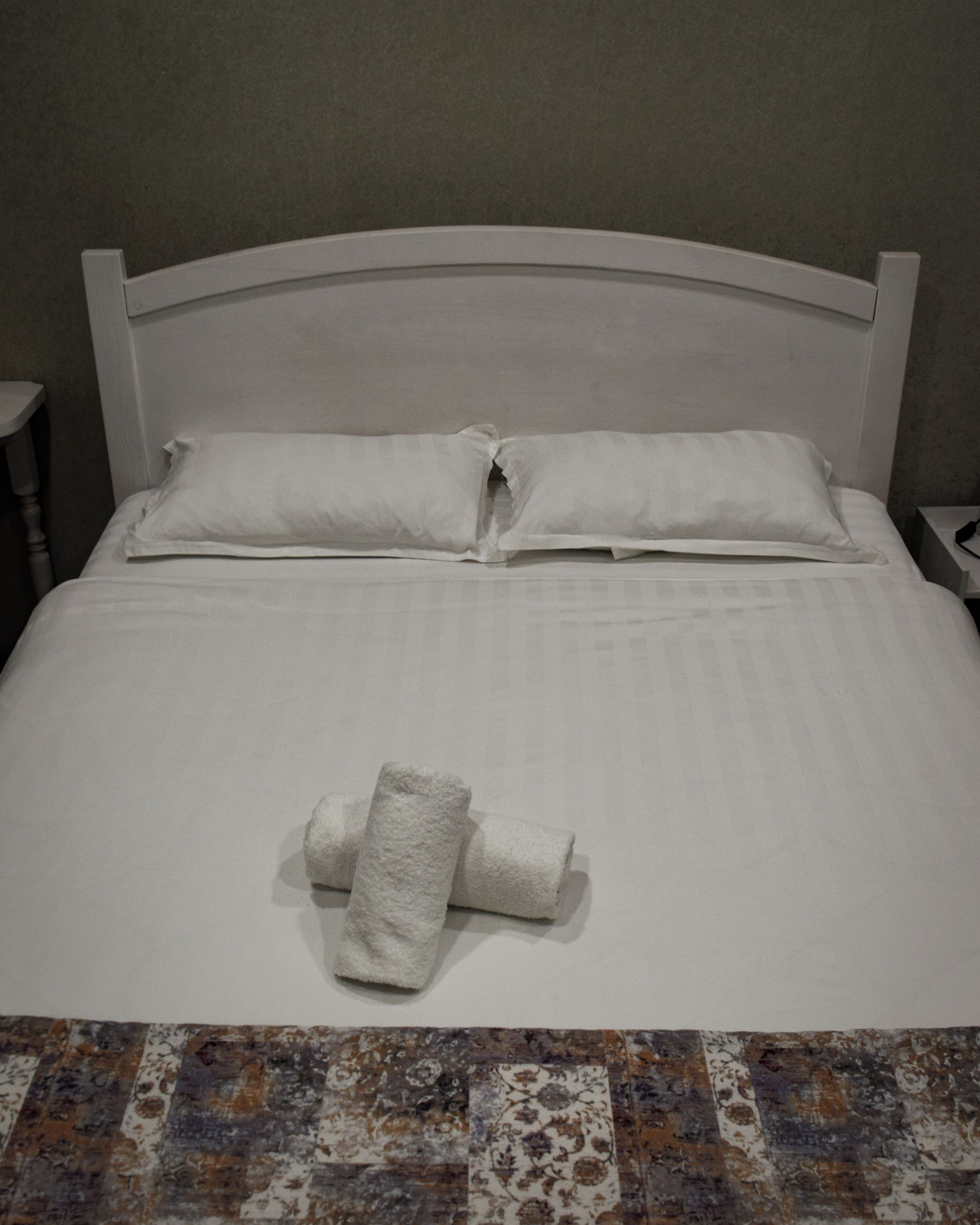 Una cama bien tendida con sábanas blancas y una toalla doblada sobre ella.