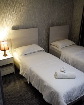 A hotel room with two single beds, a nightstand with a lamp, and a textured wall.