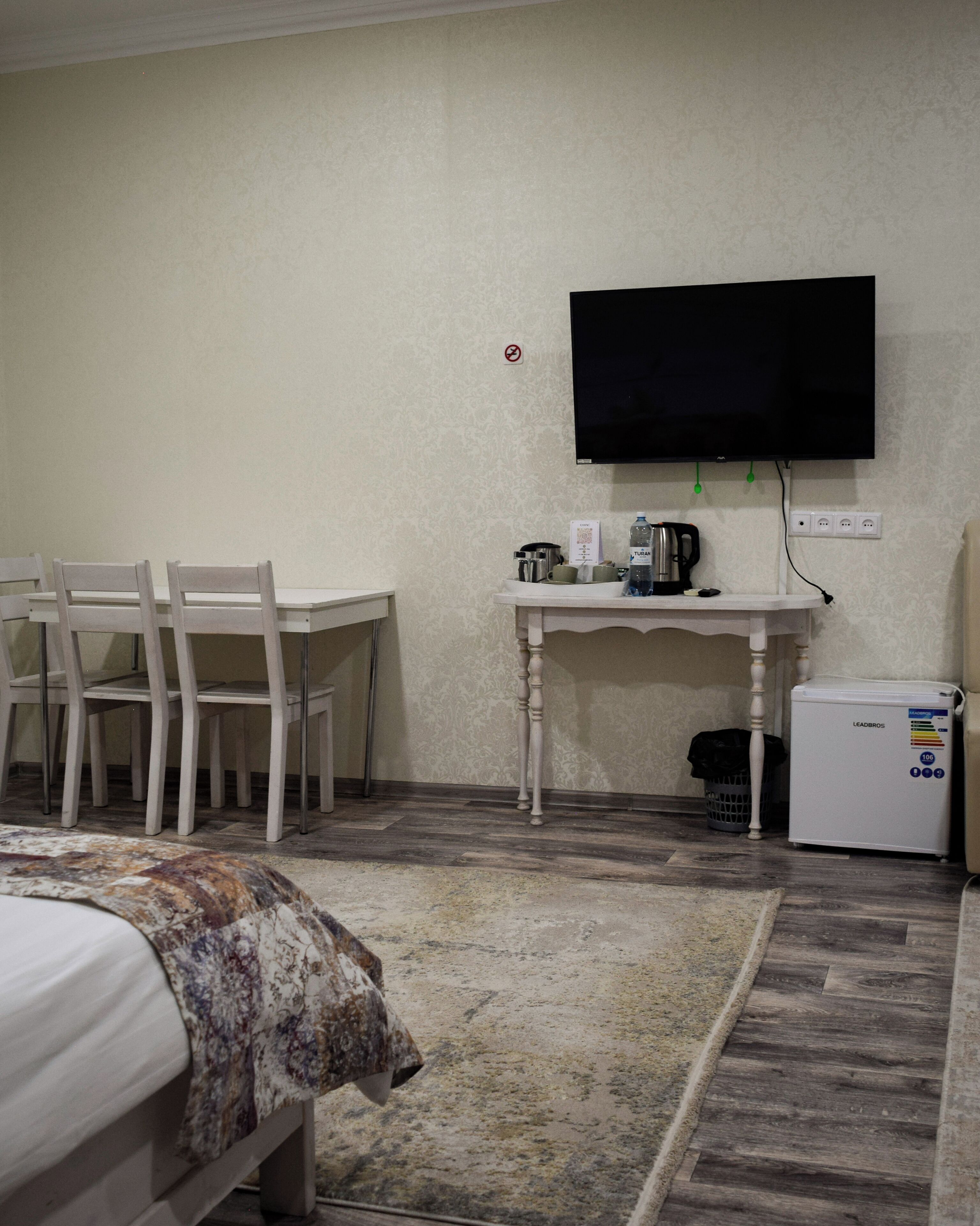 A hotel room with a bed, a desk with a chair, a television mounted on the wall, a coffee maker, and a small refrigerator.