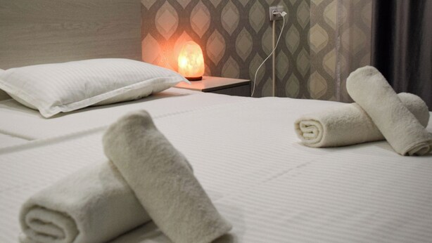 A neatly made bed with white linens and rolled towels, a headboard, and a wall with a geometric pattern. - Continent (Karagandy)