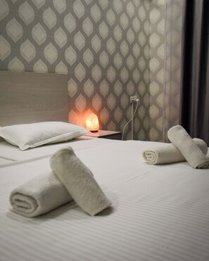 A neatly made bed with white linens and rolled towels, a headboard, and a wall with a geometric pattern. - Continent (Karagandy)