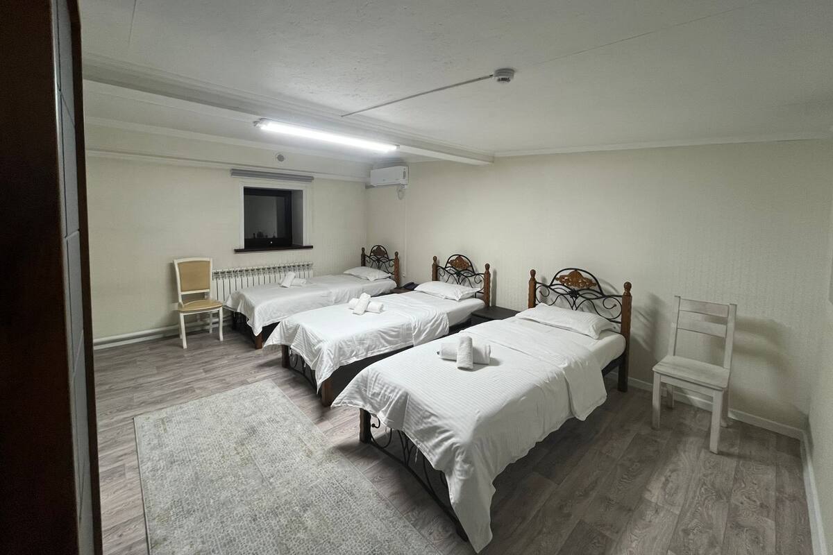 Una habitación con tres camas individuales, un ventanal pequeño, un radiador y una silla.