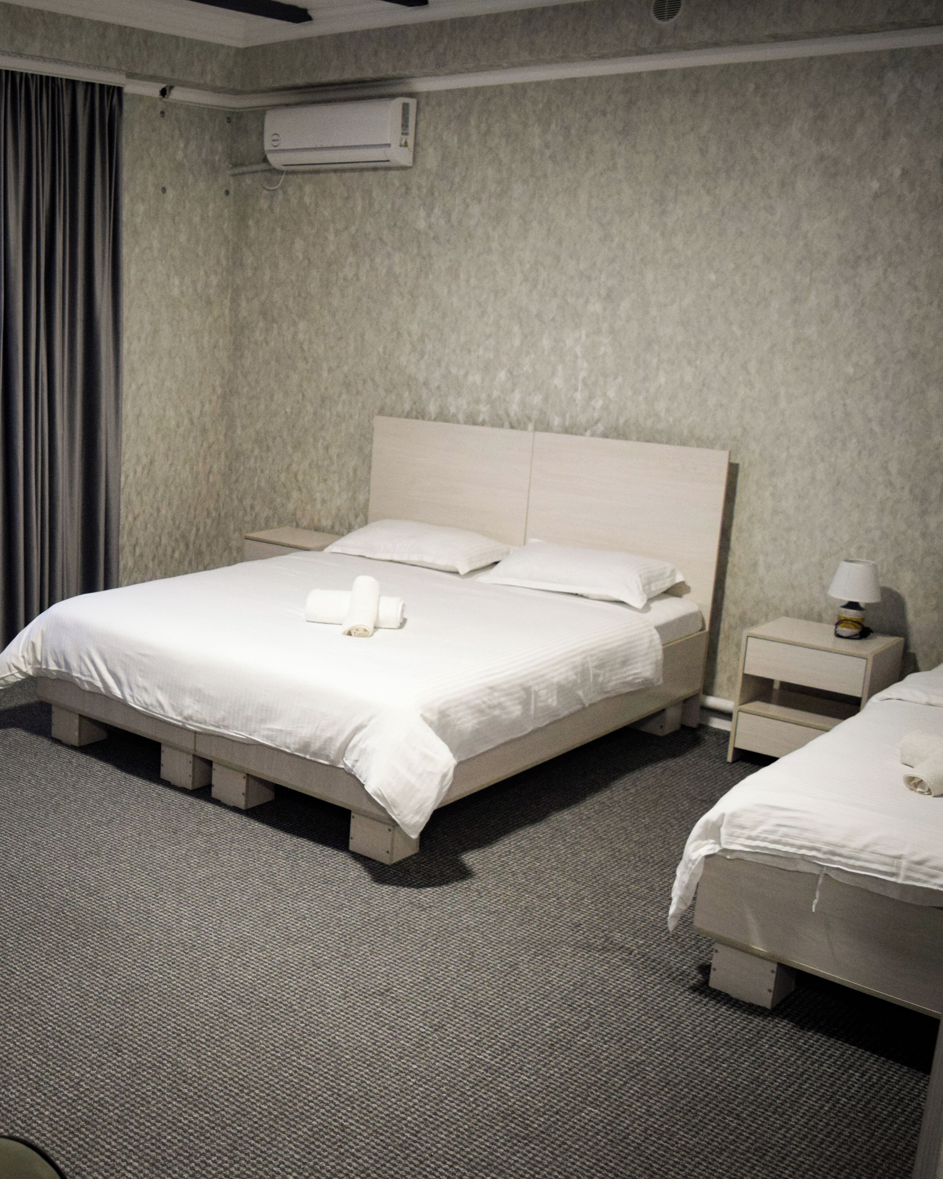 Een hotelkamer met een groot bed, een nachtkastje, een lamp en een airconditioner aan de muur.