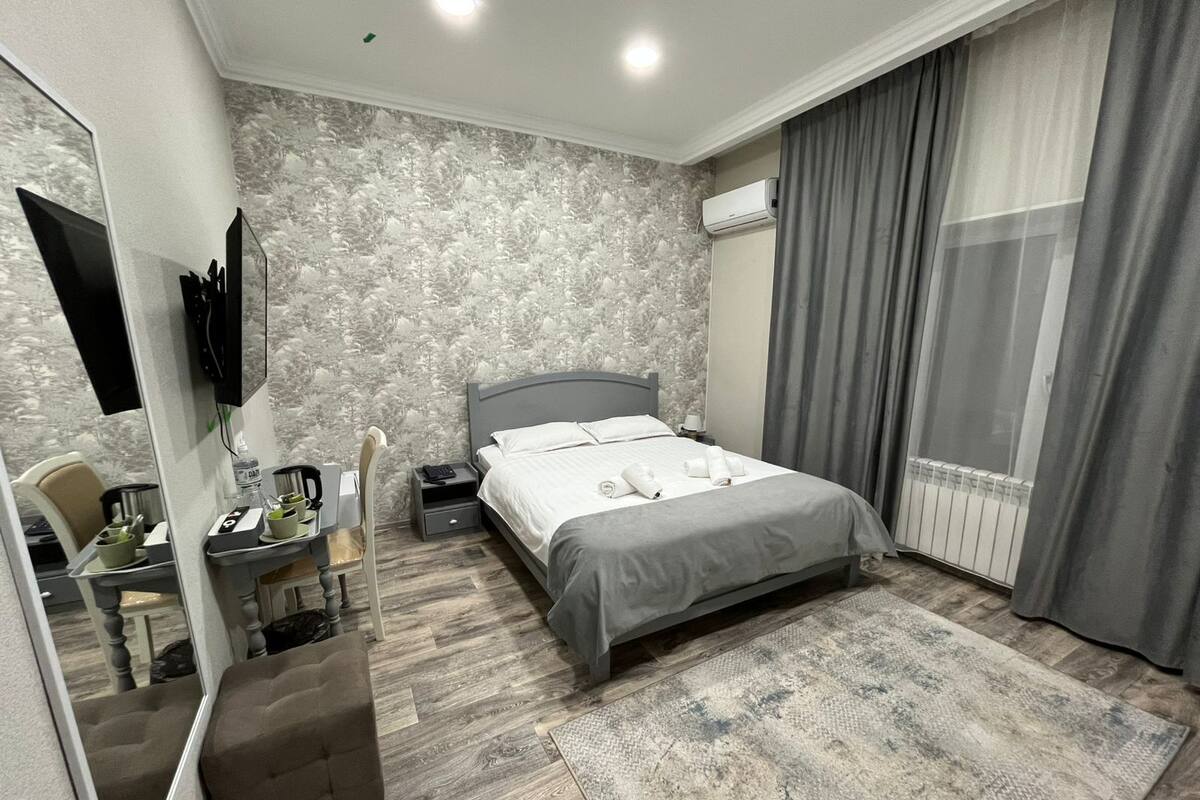 Una habitación de hotel moderna con una cama grande, un escritorio con una silla, un espejo y un televisor.