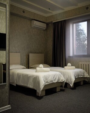 A hotel room with two beds, a window, and an air conditioning unit.