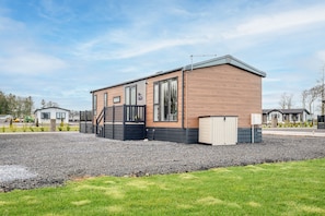 Une maison mobile moderne, avec une façade en bois, un balcon et une allée gravillonnée.