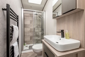 A modern bathroom with a glass shower enclosure, a white sink, and a towel rack. - Lodge No 74 | Stewart's Resort Cameron (Cameron)